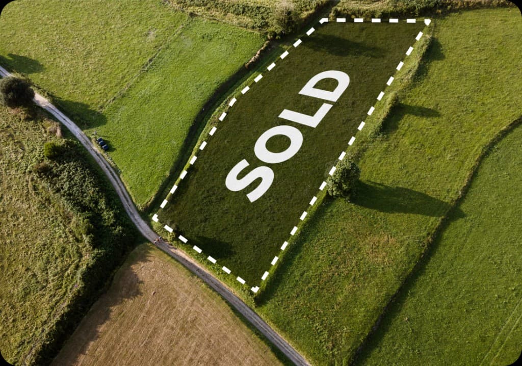 Aerial view of a sold land parcel outlined on a green field
